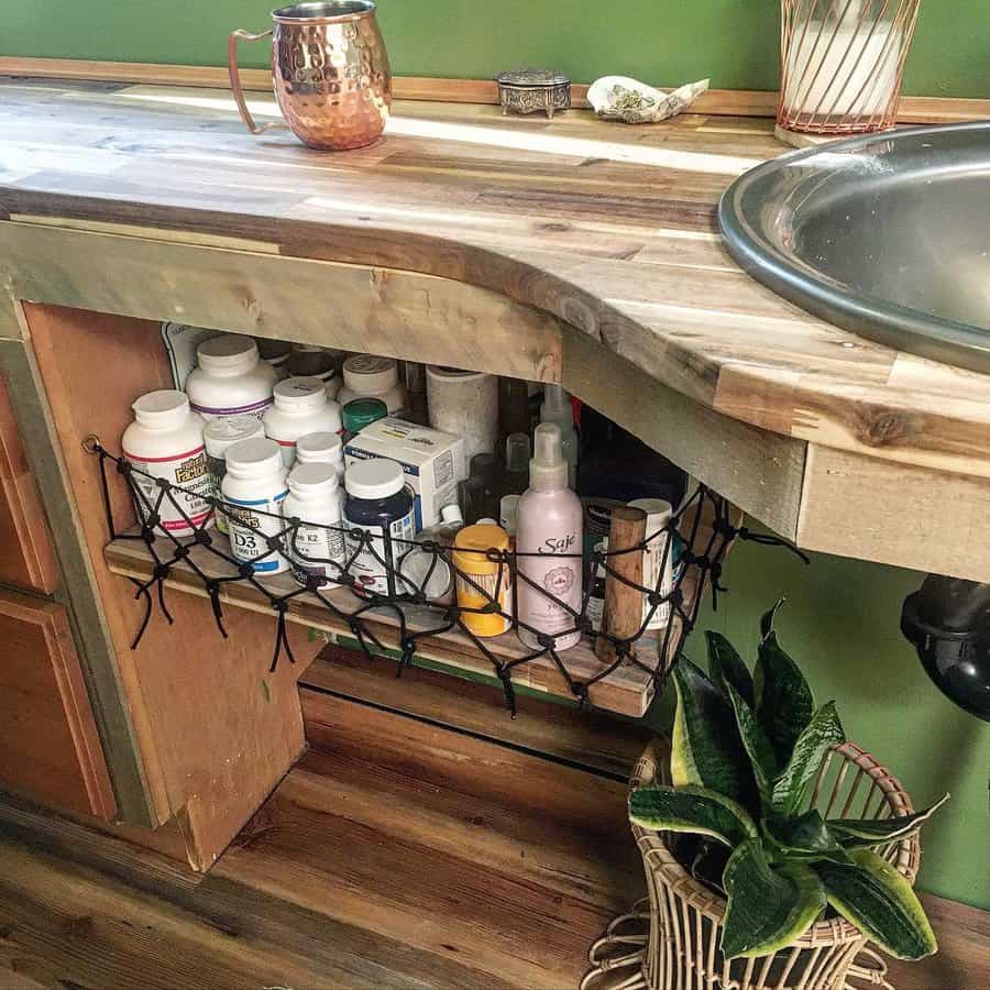 Rustic RV bathroom with an open storage shelf secured by netting, holding vitamins and toiletries, alongside a wood countertop and sink.