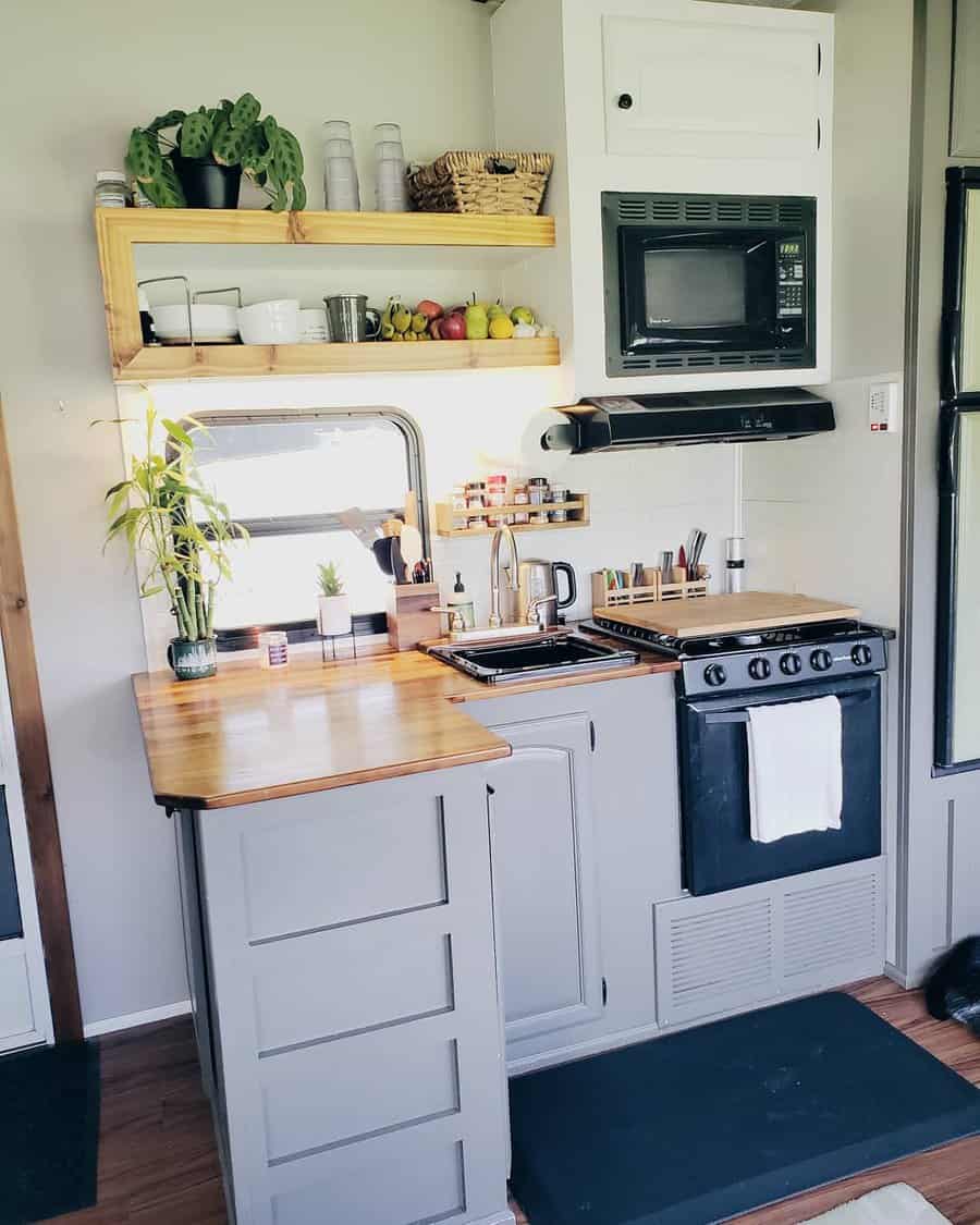 Modern RV kitchen with wood countertops, open shelves for storage, a built-in microwave, and neatly organized spices and utensils.