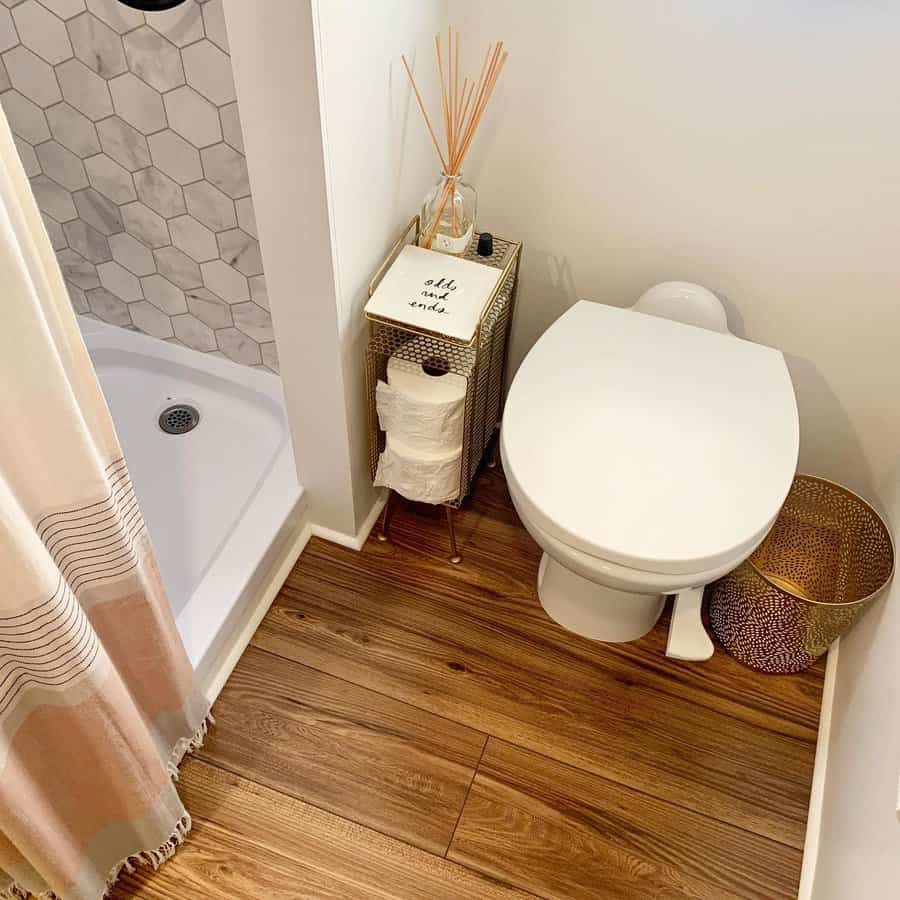 Minimalist RV bathroom with a compact shower, a sleek white toilet, and a small metal storage stand for toiletries and toilet paper.