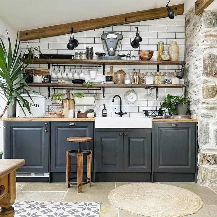 Rustic kitchen with black cabinets, open wooden shelves, subway tile backsplash, and exposed beams for a cozy farmhouse feel