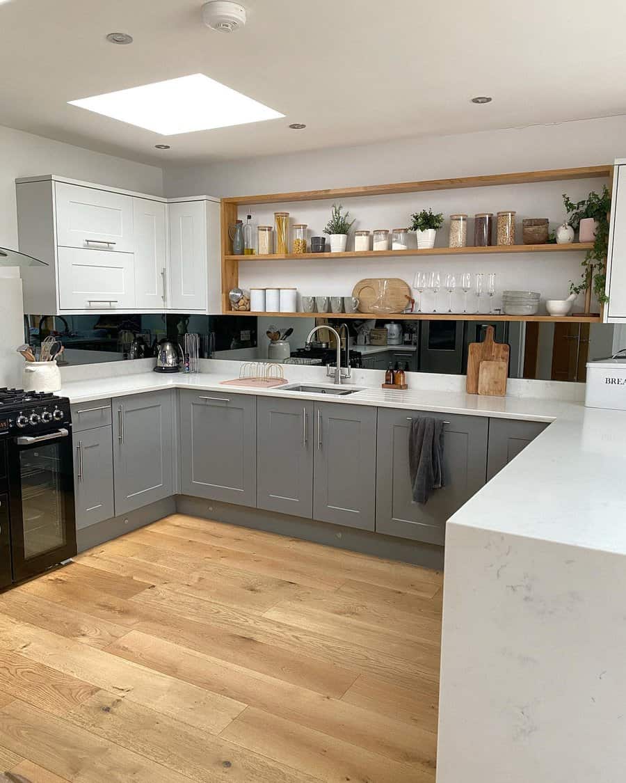 Modern kitchen with gray and white cabinets, open wooden shelves, a sleek backsplash, and natural light from a skylight