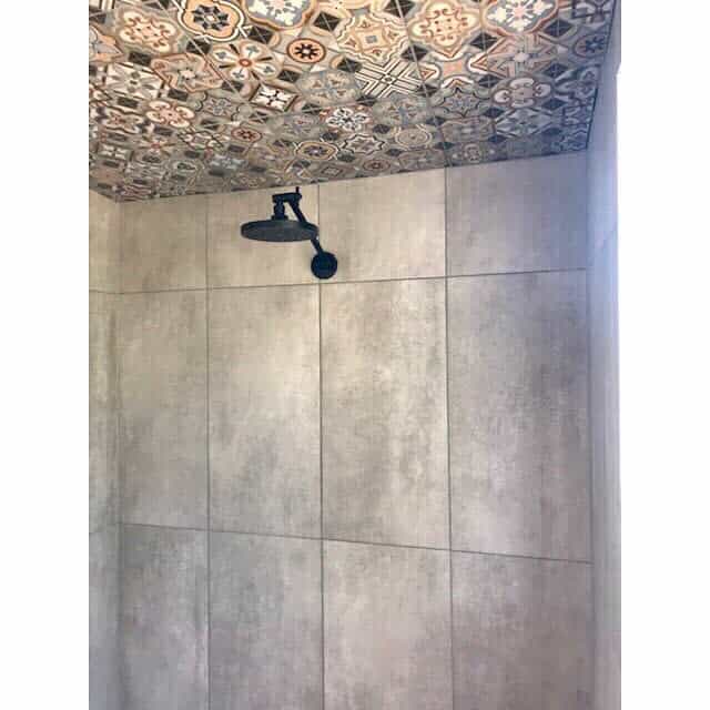 Modern shower with a bold patterned tile ceiling, concrete-style walls, and a black rain showerhead, creating a unique and stylish contrast.