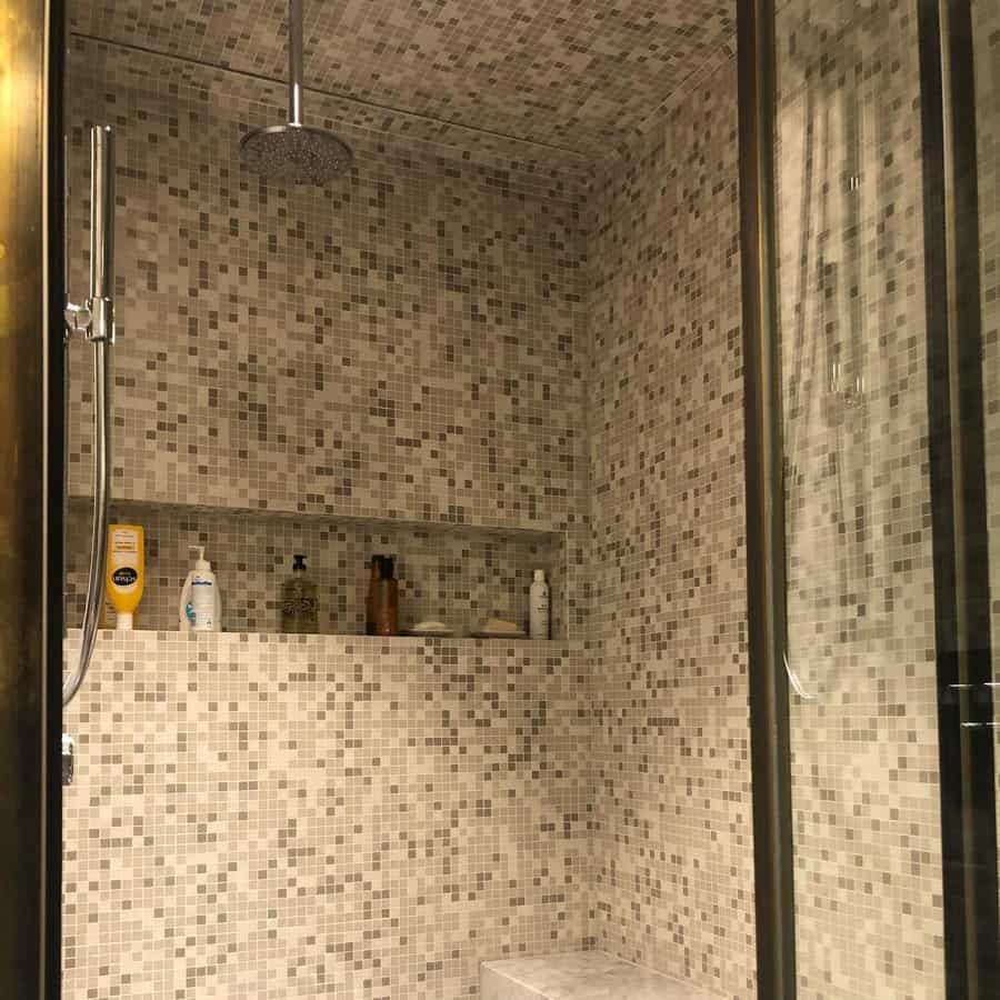 Luxurious shower with mosaic tile covering the walls, ceiling, and built-in shelves, creating a seamless spa-like retreat with a rainfall showerhead.