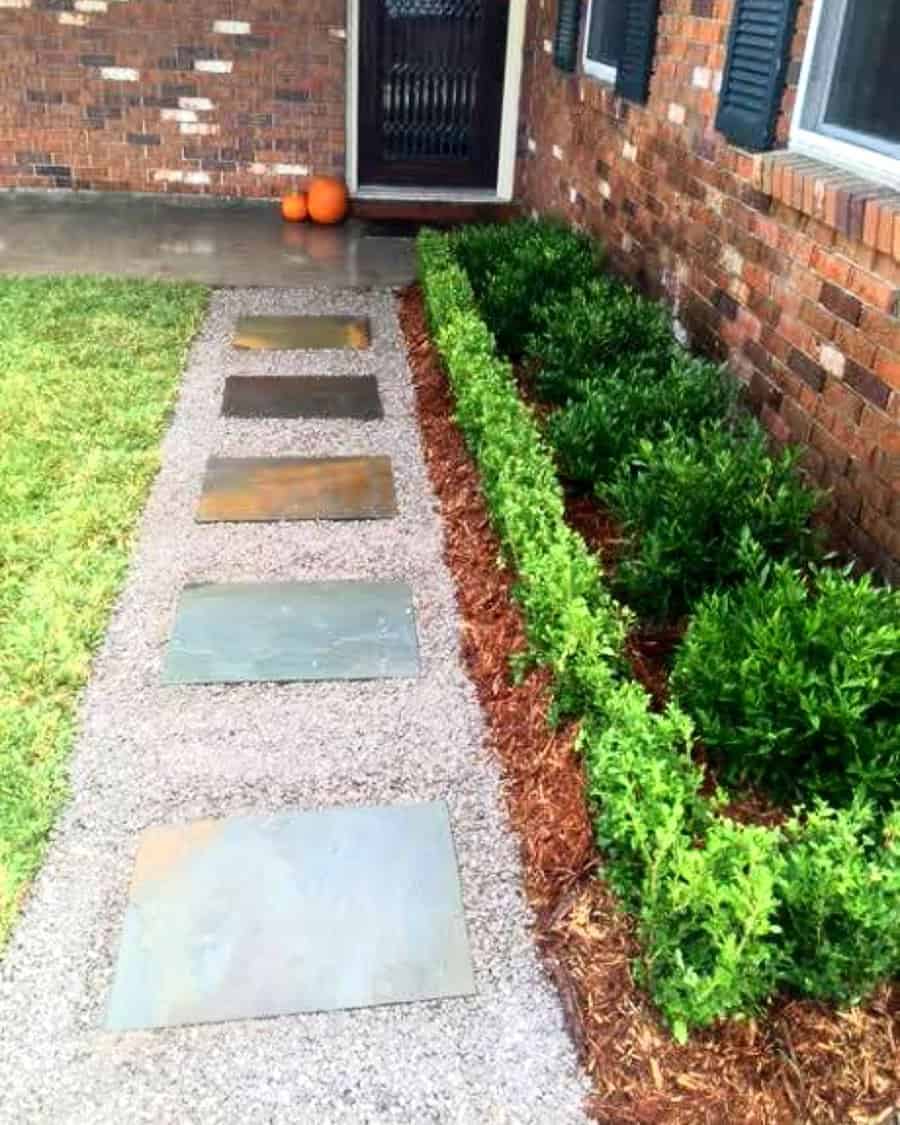 Stone pathway beside hedges, leading to a brick house entrance