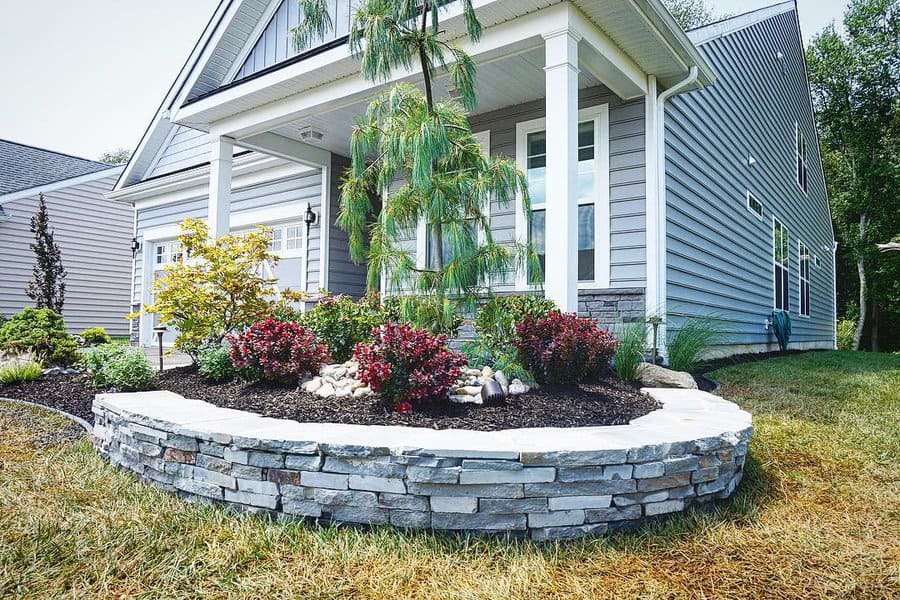 House with grey siding and stone landscaping, front yard garden with shrubs and small trees