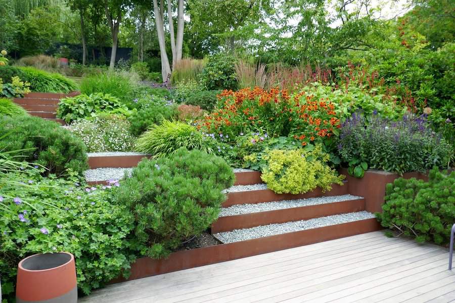 Garden scene with tiered flower beds, vibrant flowers, greenery, and a wooden deck in the foreground