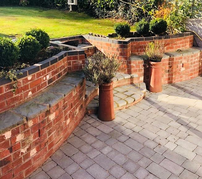 Curved brick patio with tiered garden beds, stone steps, and large potted plants