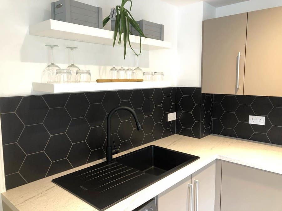 Modern kitchen corner with black hexagonal backsplash, white countertops, single black sink, shelves with glasses, and a potted plant