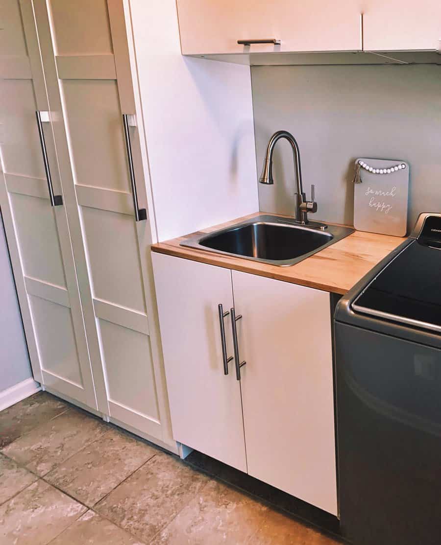 Small kitchen with a sink, wooden countertop, white cabinets, and a gray appliance, tile flooring and a "laundry" sign on the wall