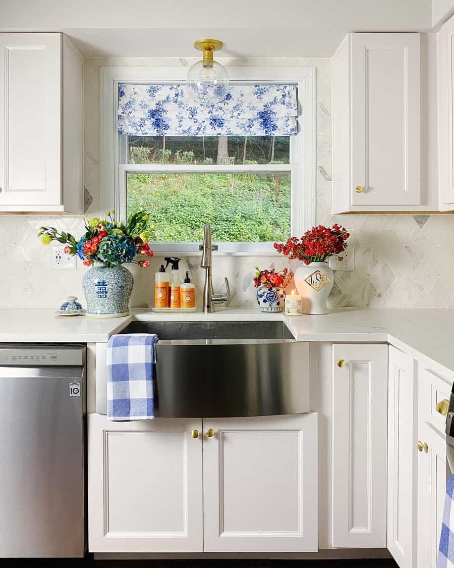 Bright kitchen with white cabinets, stainless steel farmhouse sink, patterned floral curtains, and colorful flowers on the counter