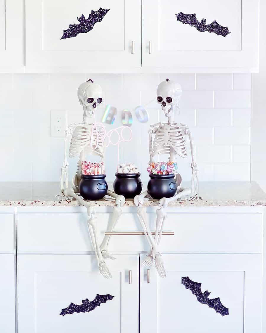 Two skeletons on a counter with candy cauldrons and bat decorations