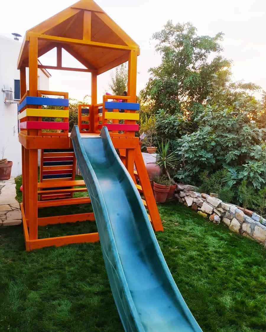 Wooden playground set with a blue slide and colorful climbing bars in a green garden