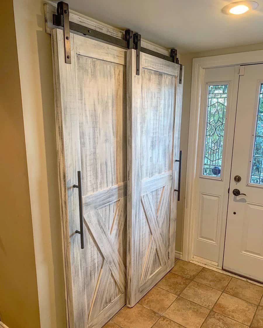 Sliding barn-style wooden doors with black handles, next to a white door with glass panels, in a tiled hallway