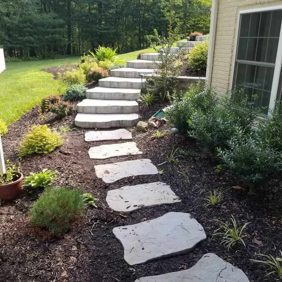 Rustic stone pathway and staircase in a slope garden with surrounding greenery and shrubs near a house