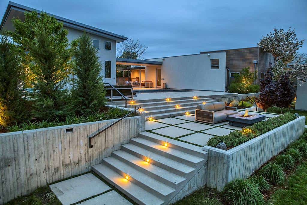 Modern house exterior at twilight featuring a lit pathway, steps, and spacious patio with contemporary design and surrounding greenery