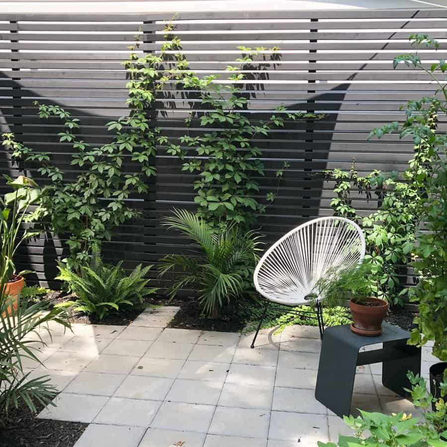 Patio with white chair, small table with potted plant, surrounded by lush greenery and a modern slatted privacy fence