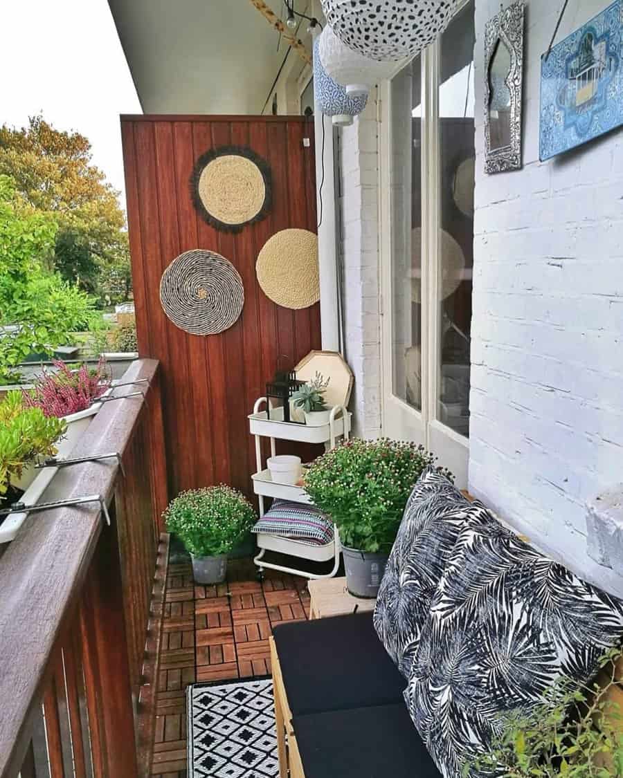 Cozy balcony with a small bench, patterned cushions, potted plants, wall decor, and a wooden floor, garden view in the background