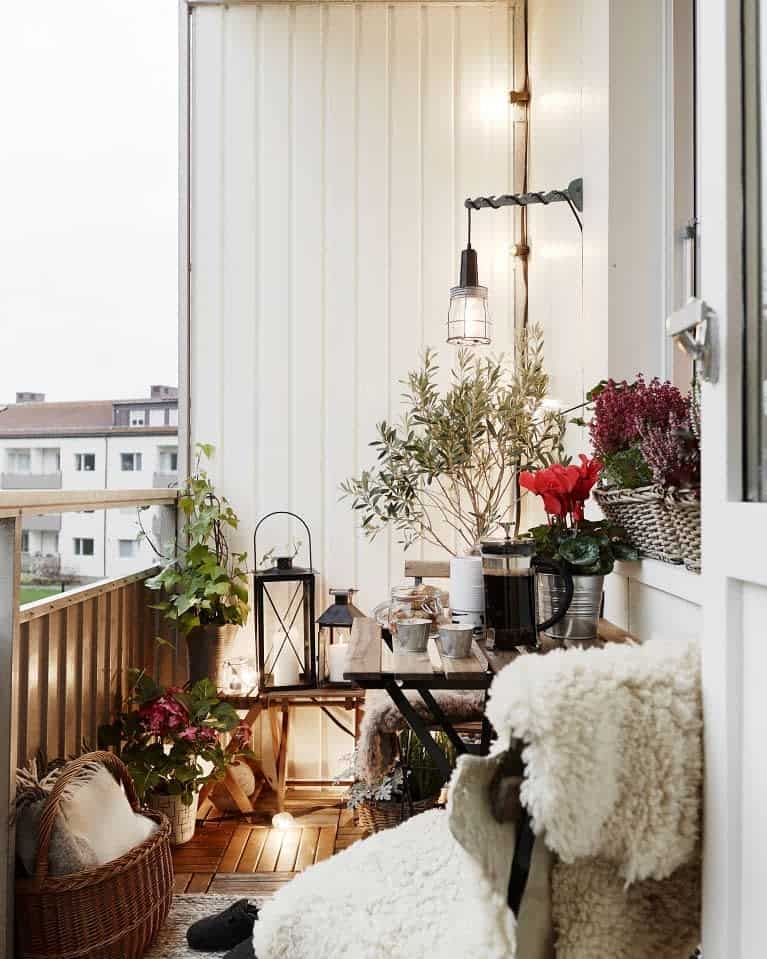 Charming small balcony with cozy seating, soft sheepskin throws, lantern lighting, and lush greenery, creating a warm and inviting retreat