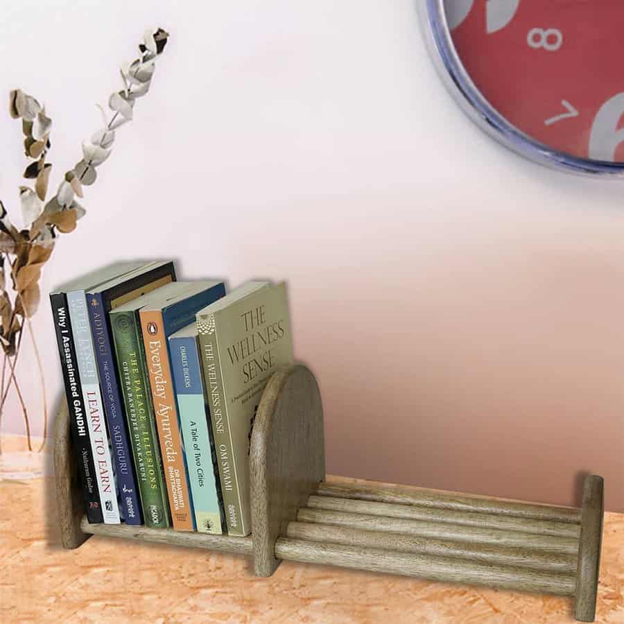 Minimalist wooden book rack holding a small collection of books on wellness and learning, placed on a wooden surface against a neutral wall.