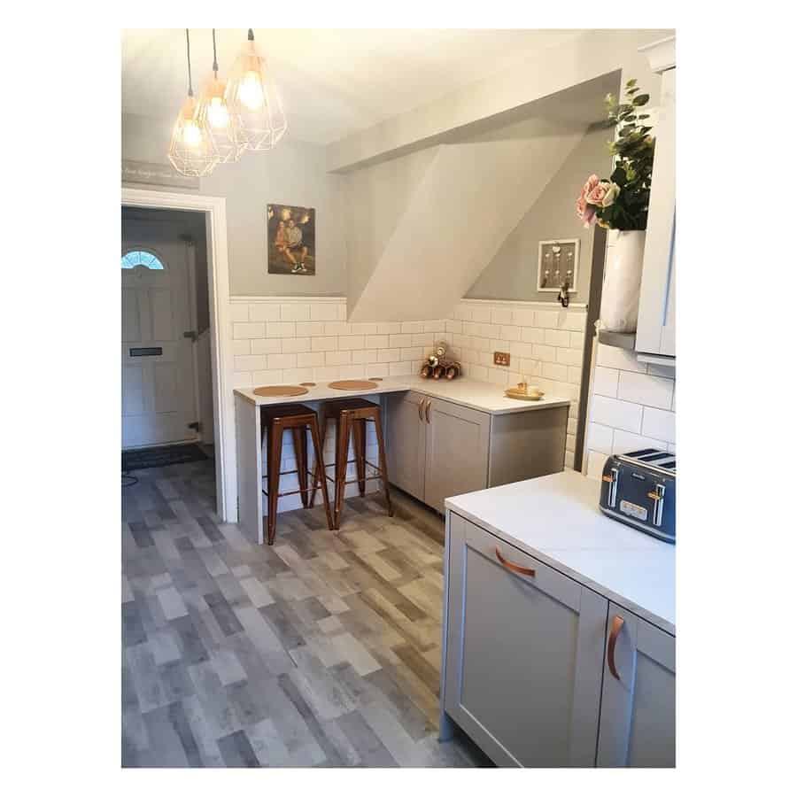 Cozy small kitchen with a built-in breakfast bar, industrial-style barstools, subway tile backsplash, soft gray cabinetry, and warm pendant lighting