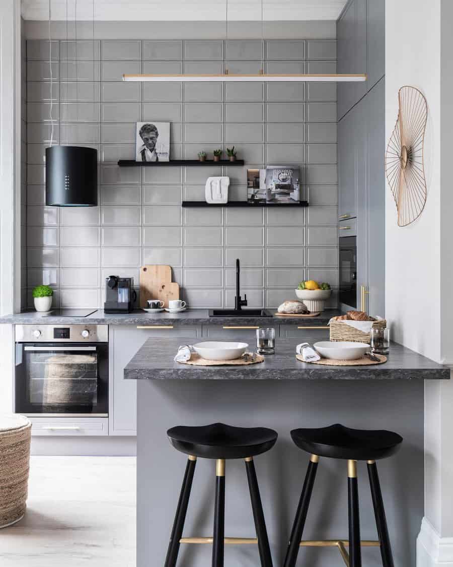 Stylish small kitchen with a gray breakfast bar, black and gold barstools, modern tiled backsplash, open shelving, and sleek pendant lighting