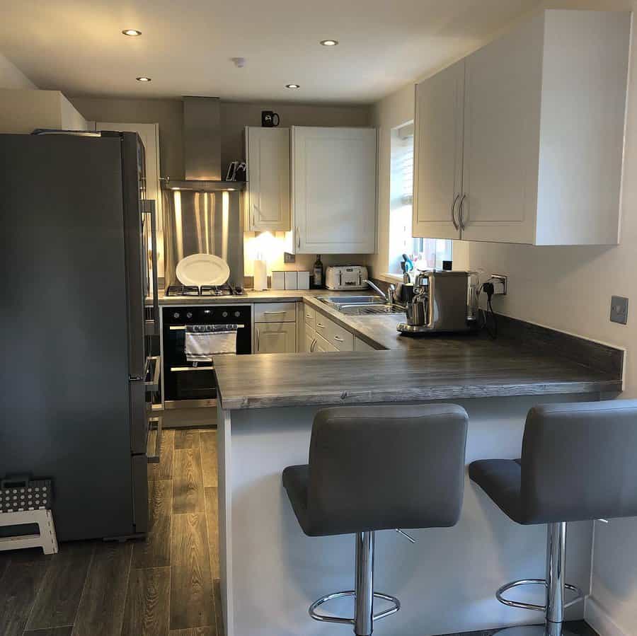 Compact kitchen with a stylish small breakfast bar, dark wood countertop, gray barstools, white cabinetry, and stainless steel appliances for a modern touch