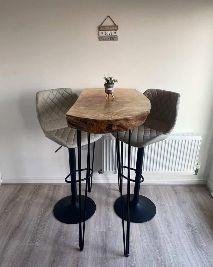 Cozy small breakfast bar with a rustic live-edge wooden table, quilted gray barstools, sleek black metal legs, and a minimalist decor setup