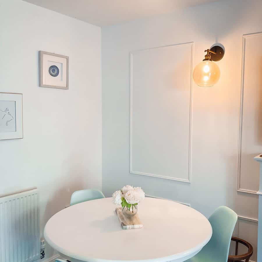 Minimalist dining area with a round white table, pastel green chairs, wall art, and a glowing wall sconce