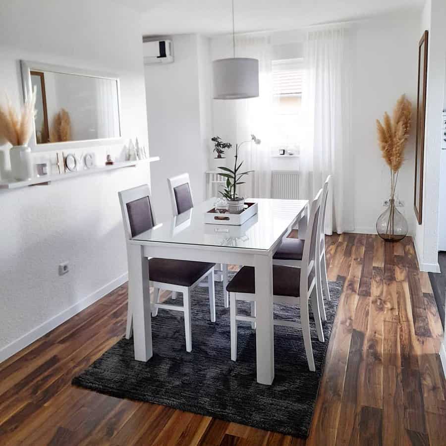 Modern dining room with a glass-top white table, four chairs, wood flooring, a rug, a mirror, and pampas grass decor