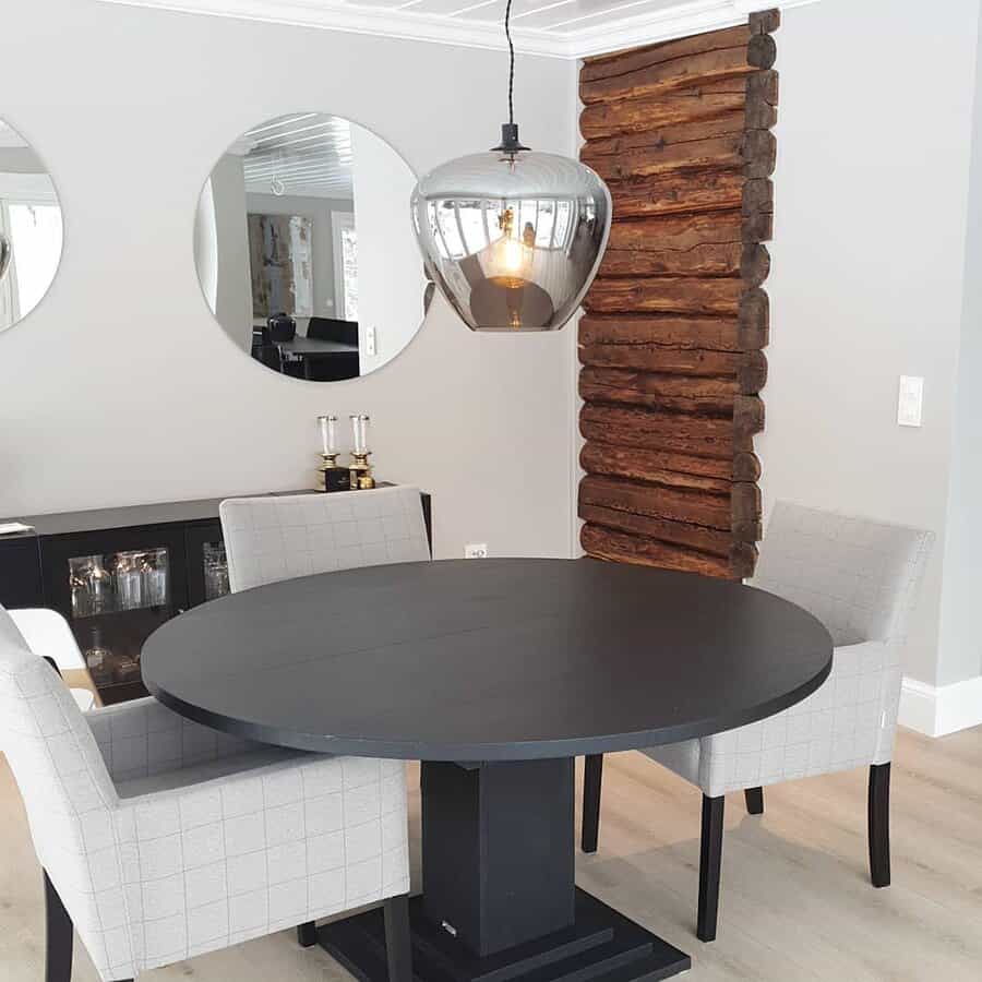 Modern dining area with a round black table, two upholstered chairs, wood accent wall, and a hanging glass pendant light