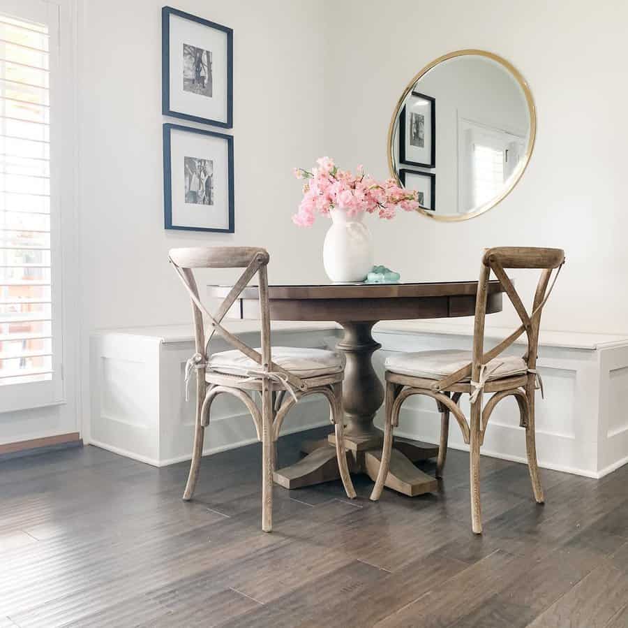 Cozy dining nook with a round wooden table, two chairs, pink flowers in a vase, and a circular mirror on the wall