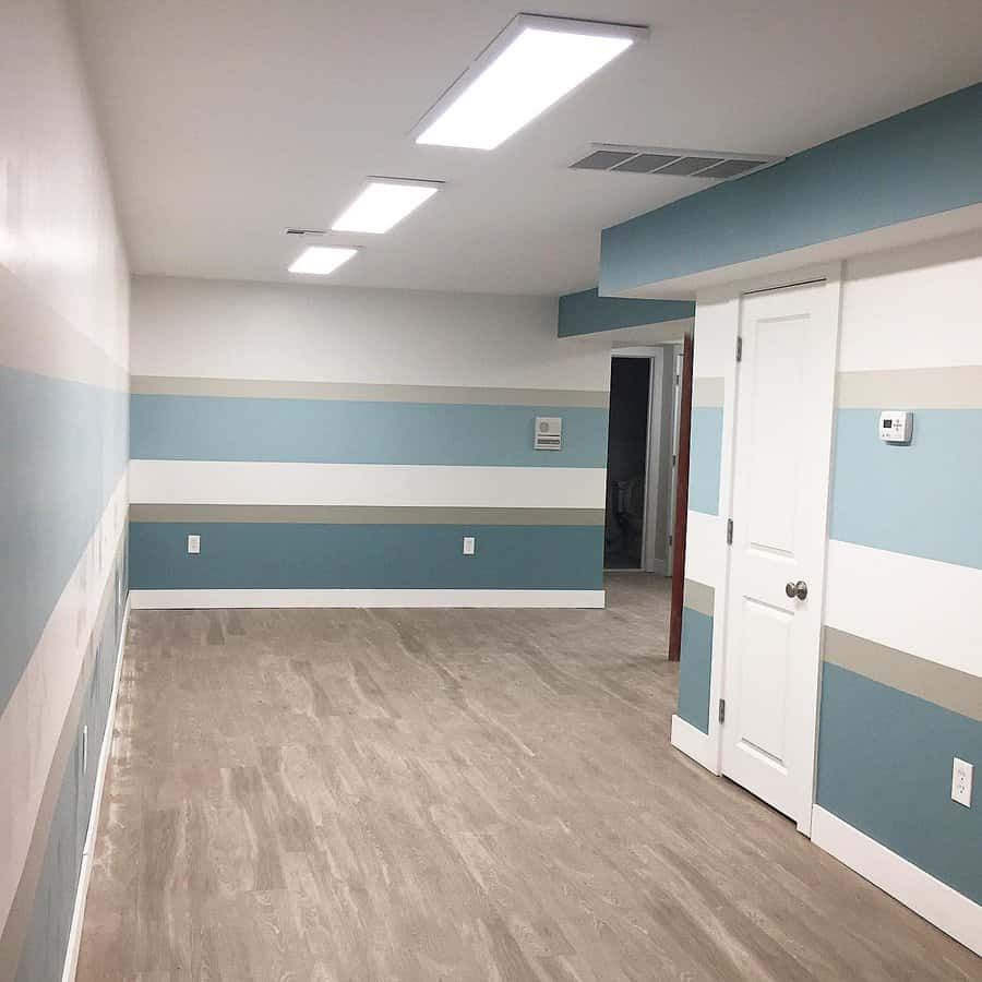 Bright and modern small basement with striped accent walls, recessed lighting, and wood-look flooring for a clean and spacious feel.