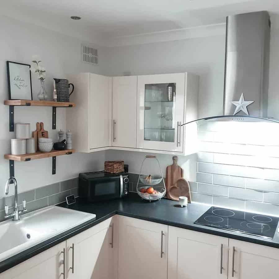 Modern kitchen with white cabinets, black countertop, electric stove, microwave, sink, and decorative items on floating shelves