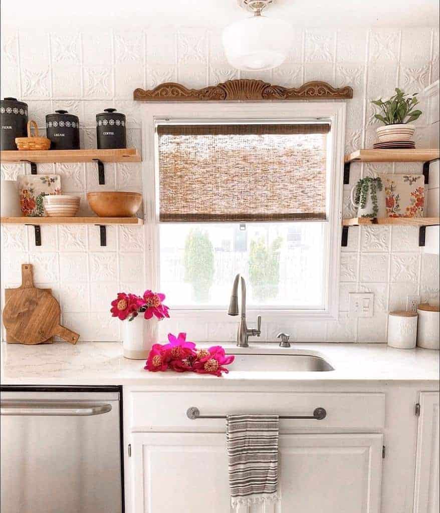 Cozy farmhouse kitchen with small wooden floating shelves, vintage tin backsplash, and rustic decor surrounding a bright sink window