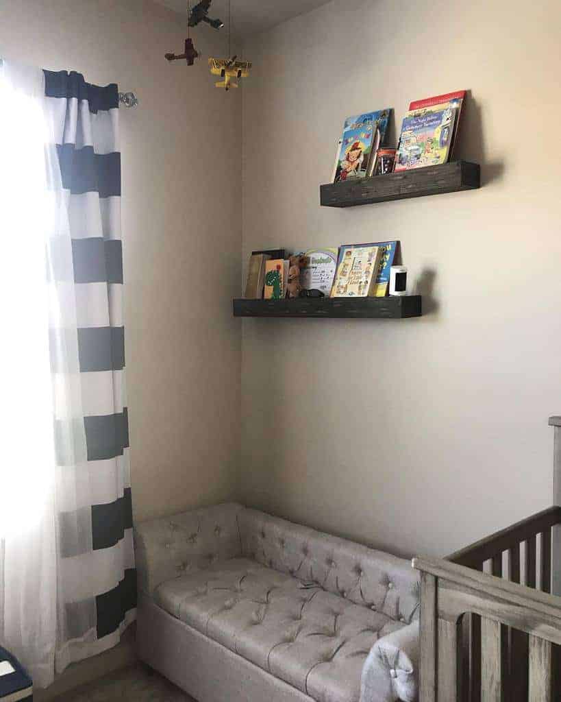 Cozy nursery corner with dark wooden floating bookshelves, a tufted sofa, and a crib, creating a charming reading nook