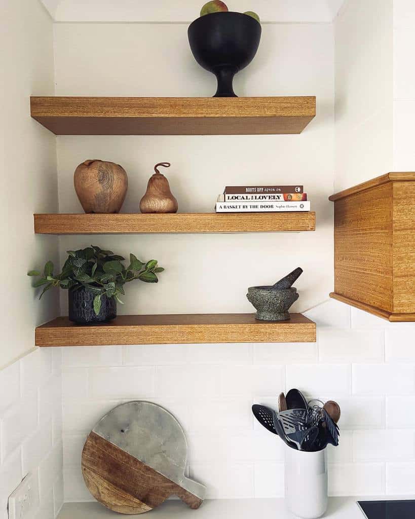 Wooden shelves with decor: a black bowl with fruit, two wooden pears, books, a plant, a mortar and pestle, and kitchen utensils