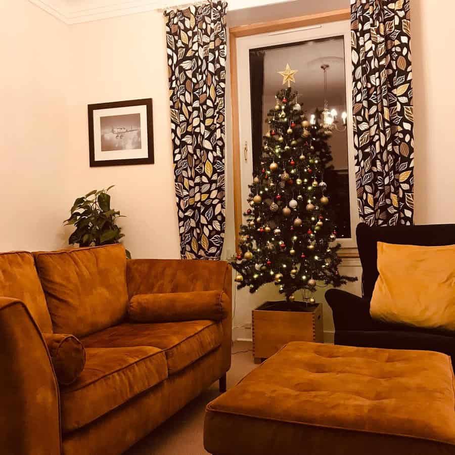 Small living room with warm mustard-toned seating, patterned curtains, a festive Christmas tree, and soft lighting for a welcoming holiday ambiance