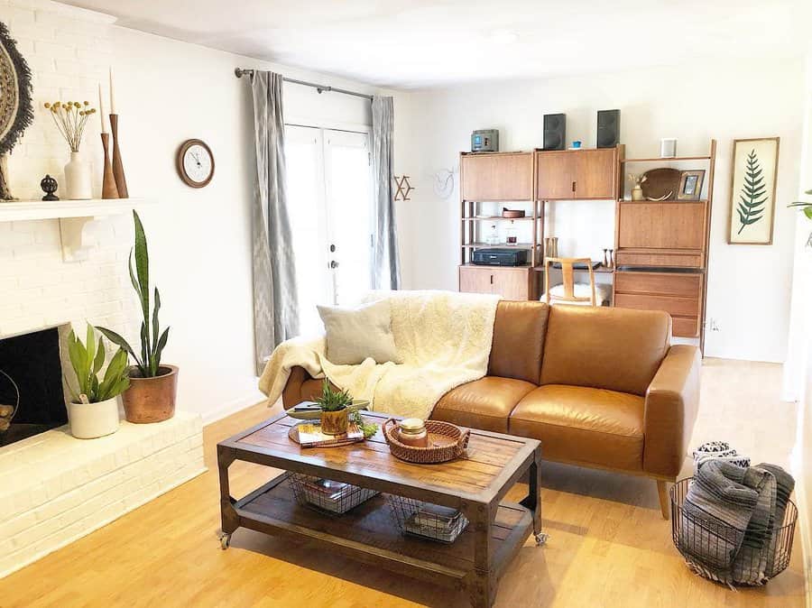 Bright small living room with a warm leather sofa, rustic wooden coffee table, white brick fireplace, and mid-century shelving for a stylish touch