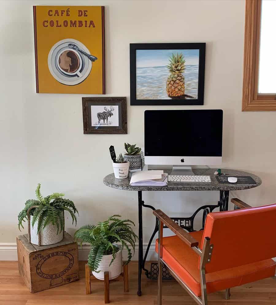 Home office with an iMac, orange chair, green plants, and wall art featuring a pineapple, moose, and a coffee-themed print