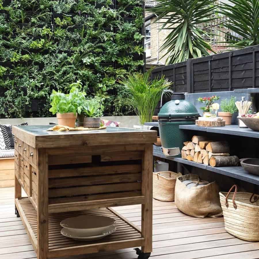 Outdoor urban patio with a wooden kitchen island, a green egg smoker, and shelves holding firewood and plants, featuring a vertical garden on walls