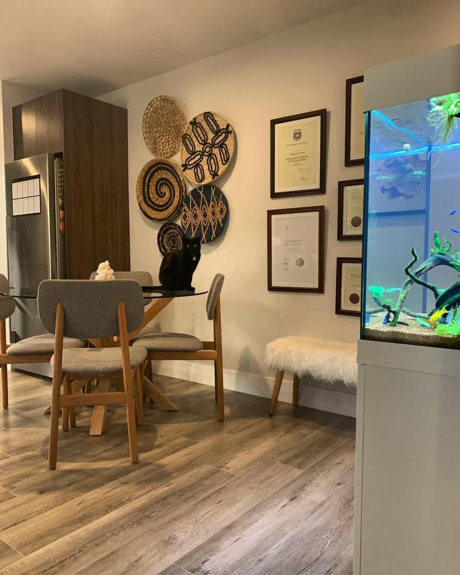 Dining area with wooden table and chairs, a black cat sitting on the table, wall art and certificates on the wall, and a fish tank