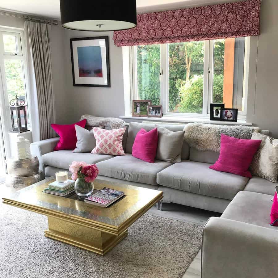 Modern living room with a gray sofa, pink accents, and a gold coffee table