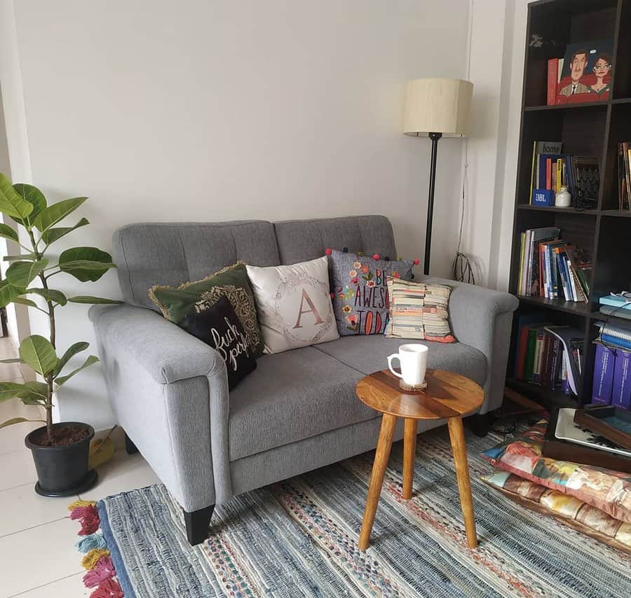 Tiny living room with a gray loveseat, colorful accent pillows, a wooden side table, a patterned rug, and a bookshelf for a warm, inviting space.