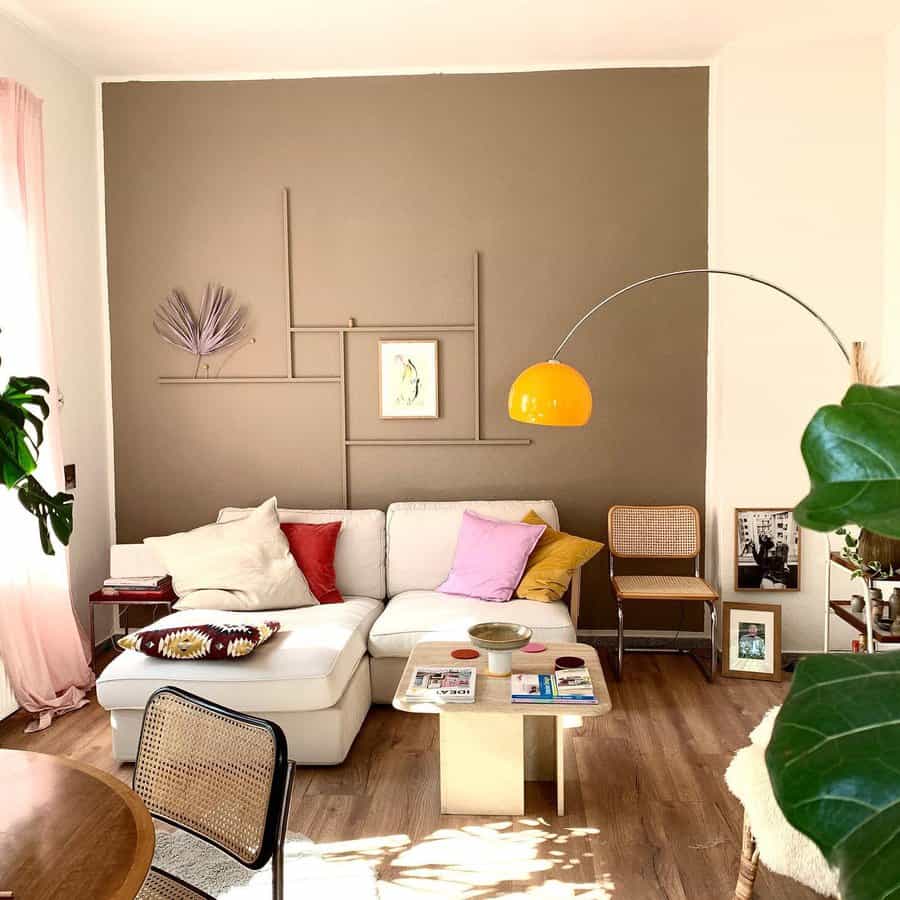 Bright living room with a white sectional sofa, colorful cushions, a yellow floor lamp, and a modern wall design with decor