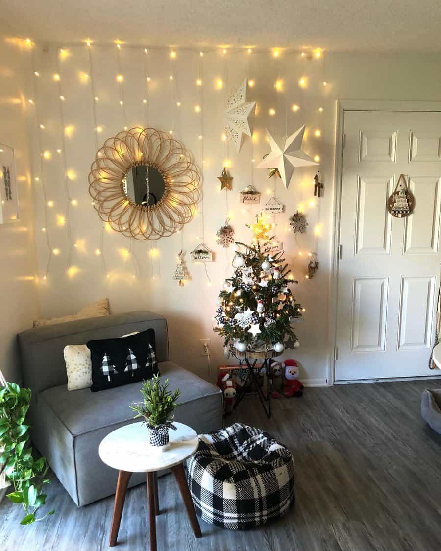 Cozy living room with a small decorated Christmas tree, string lights, star decorations, a gray chair, and a checked pouf