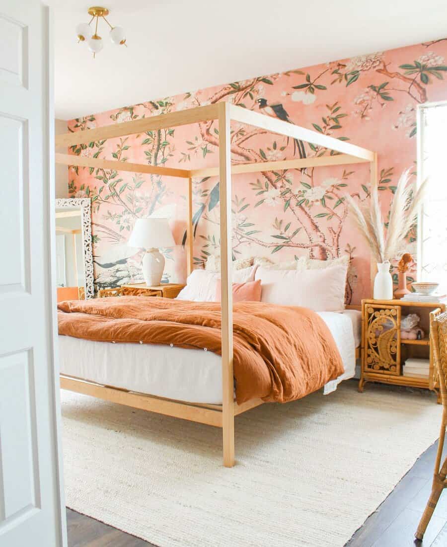 Bedroom with a wooden canopy bed, orange bedding, floral wall design, wicker nightstand, and decorative pampas grass in a vase