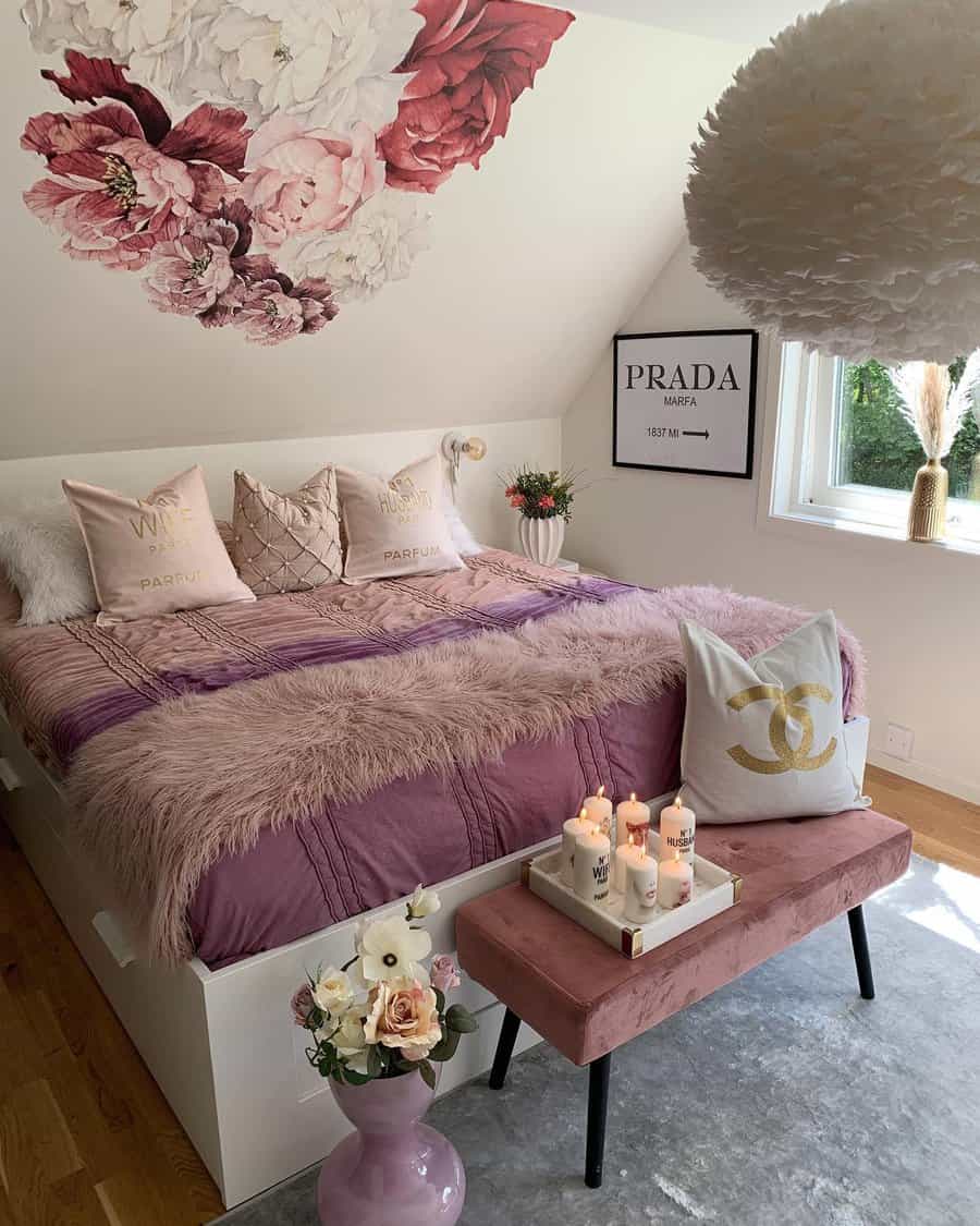 Bedroom with a purple-themed bed, floral wall art, candles, and pink bench; window with light, fluffy chandelier, and decorative pillows