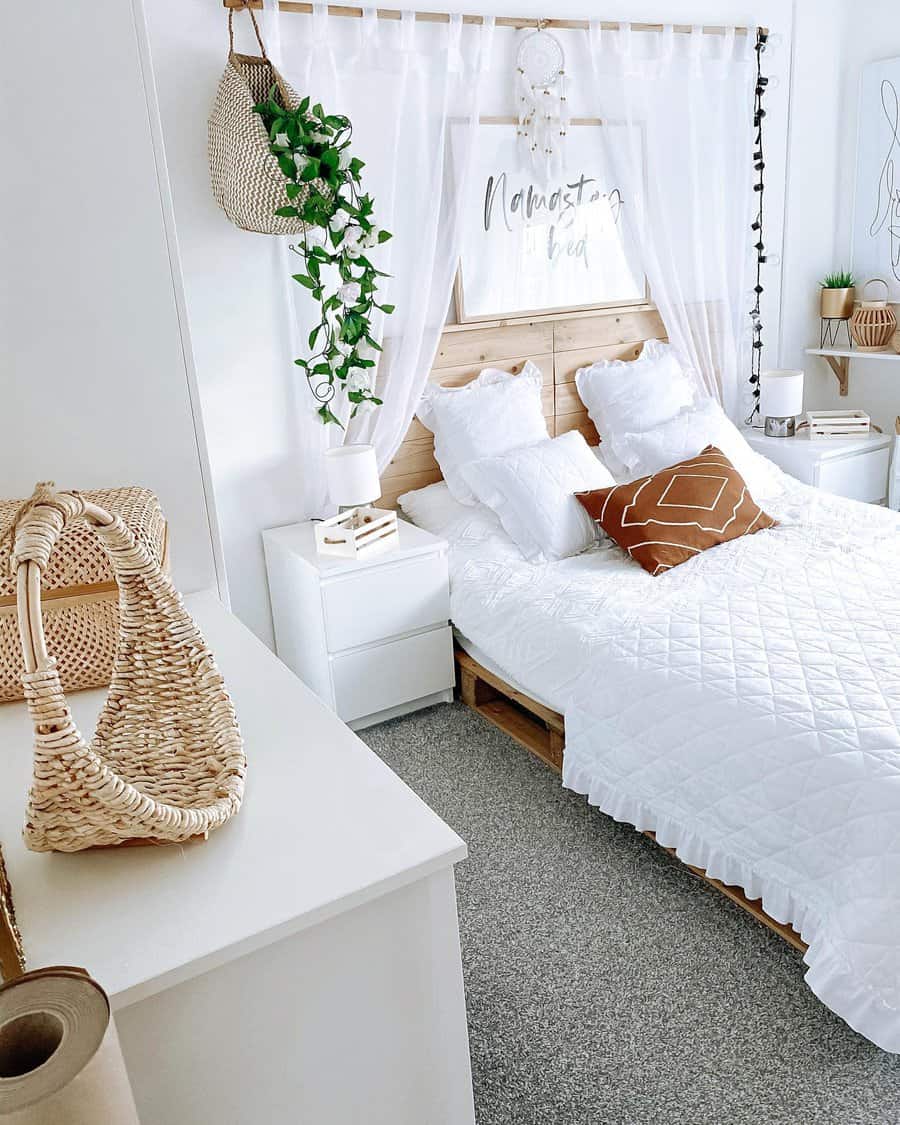 Bright bedroom with a white bed, decorative pillows, hanging plants, and a dreamcatcher; natural light and cozy decor create a serene feel