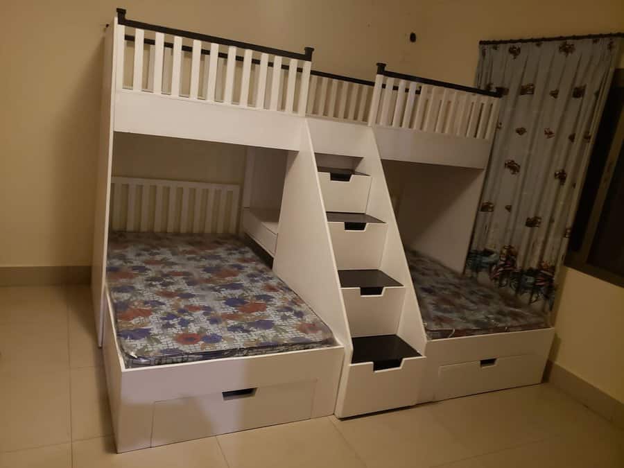 White bunk bed with a ladder and built-in storage drawers, featuring patterned mattresses, room has tiled floor and curtains with designs