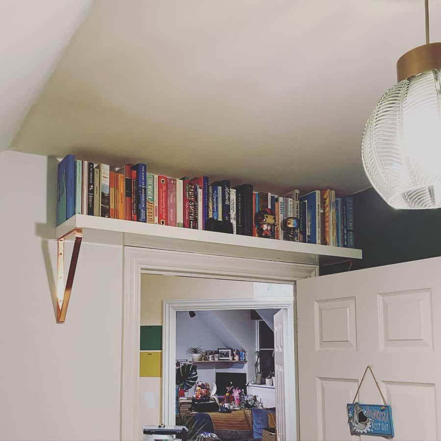 Creative space-saving bookshelf mounted above a doorway, neatly storing colorful books in a cozy, well-lit room.